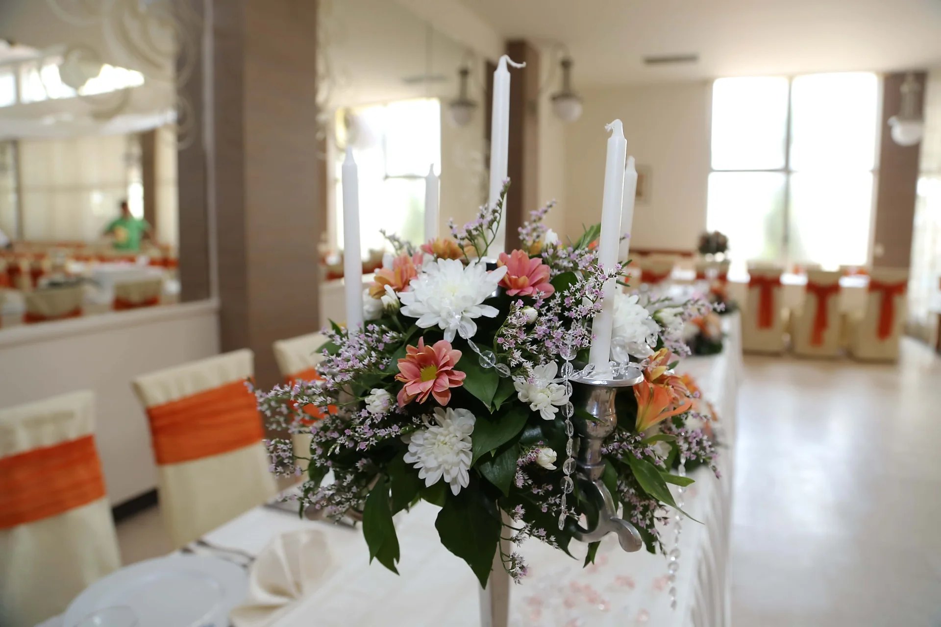 Fotografie von weissen Stabkerzen und einem Blumengesteck in Weiss, Rosa und Apricot auf einer festlichen Tafel